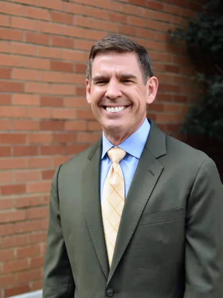 Dennis Wiese smiling in a suit and tie in front of a brick wall