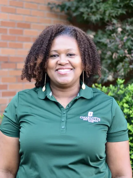 Nicole Benford smiling next to a brick wall and greenery